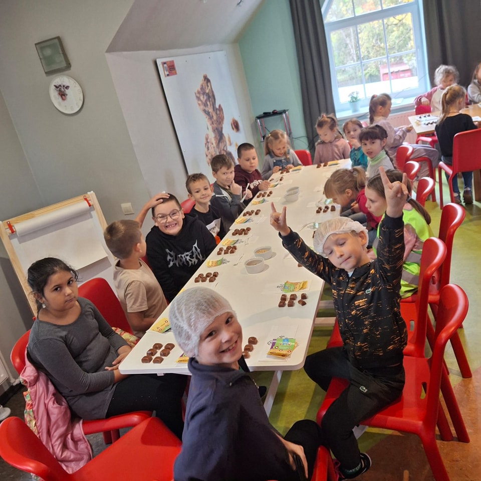 Skolēnu kopbilde, skolēni sēž ap galdu uz kura ir paštaisītas konfektes
