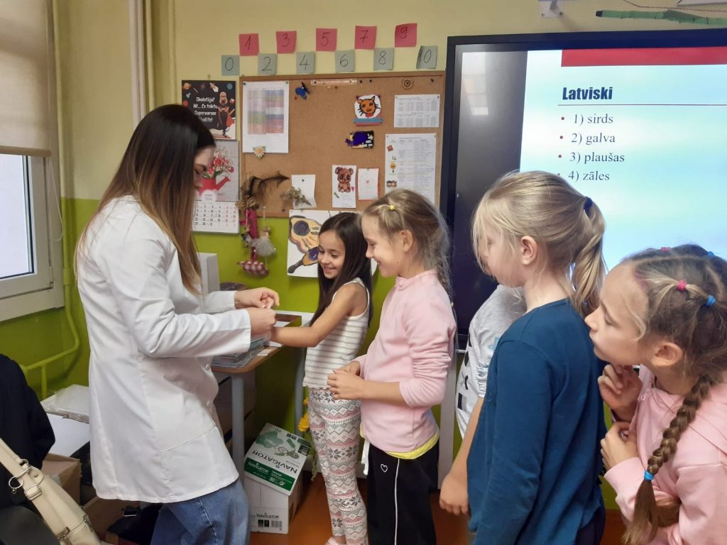 5 skolēni rindā pie dakteres, kas demonstrē procedūru